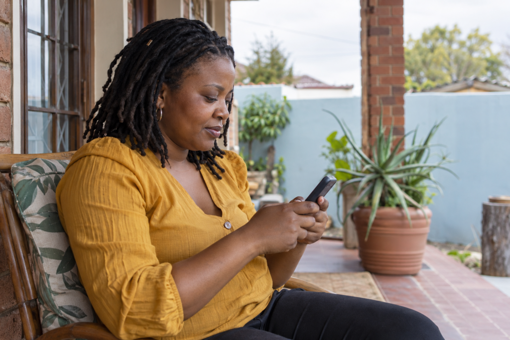 Woman using a mobile phone on a veranda, illustrating a SARS tax number via SMS guide.
