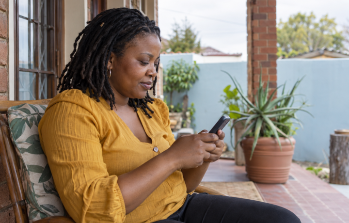 Woman using a mobile phone on a veranda, illustrating a SARS tax number via SMS guide.