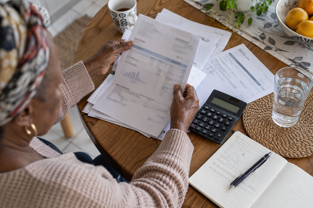 Woman reviewing household statements at a table beside a calculator and notebook